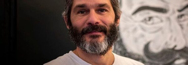 Pépé Ronchon dans sa pizzeria devant son logo